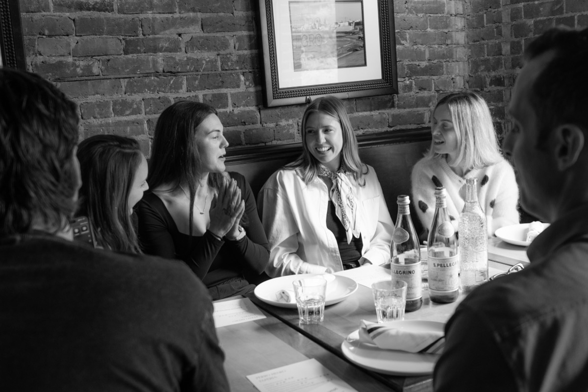 Members talking along a banquette against a brick wall